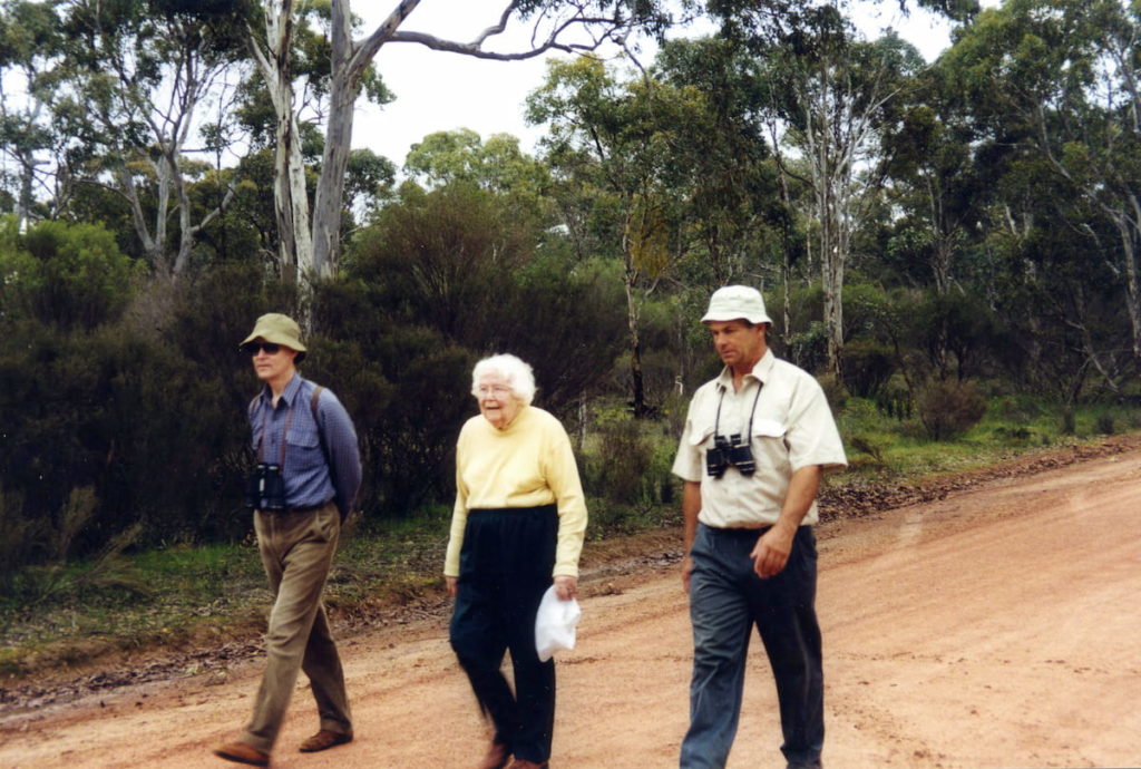 Three people walking down track through woodland with binoculars around their neck