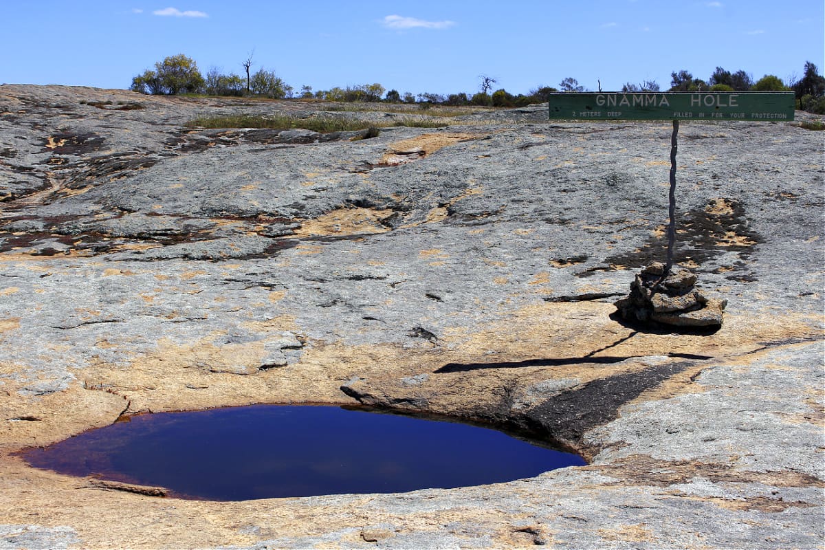 Large hole full of water in granite with sign saying gnamma hole