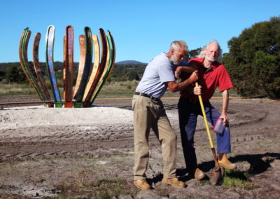 Two men rest on a shovel with installed sculpture in the background